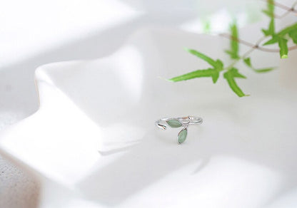 Silberner Ring mit grünen Blättern, verstellbar, auf weißem Keramikteller, Schmuckdesign.
