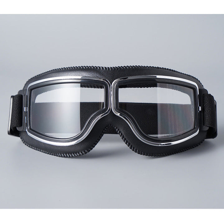 Schwarze Lederbrille mit verchromtem Rahmen, klaren Gläsern und elastischem Band, Vorderansicht vor grauem Hintergrund. 2