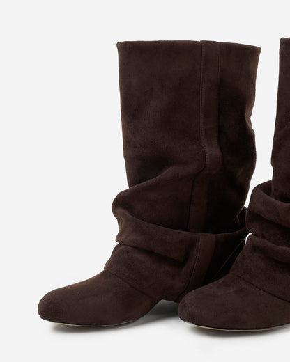 Nahaufnahme eines Paars dunkelbrauner Stiefel von vorn mit runder Spitze, Raffungen am unteren Schaft und sichtbarer Naht. 6