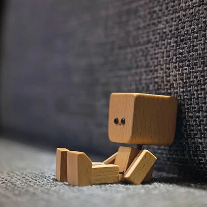 Holzfigur sitzt auf grauem Teppich und lehnt am Rücken eines dunklen, grob gewebten Stoffsofas. 7