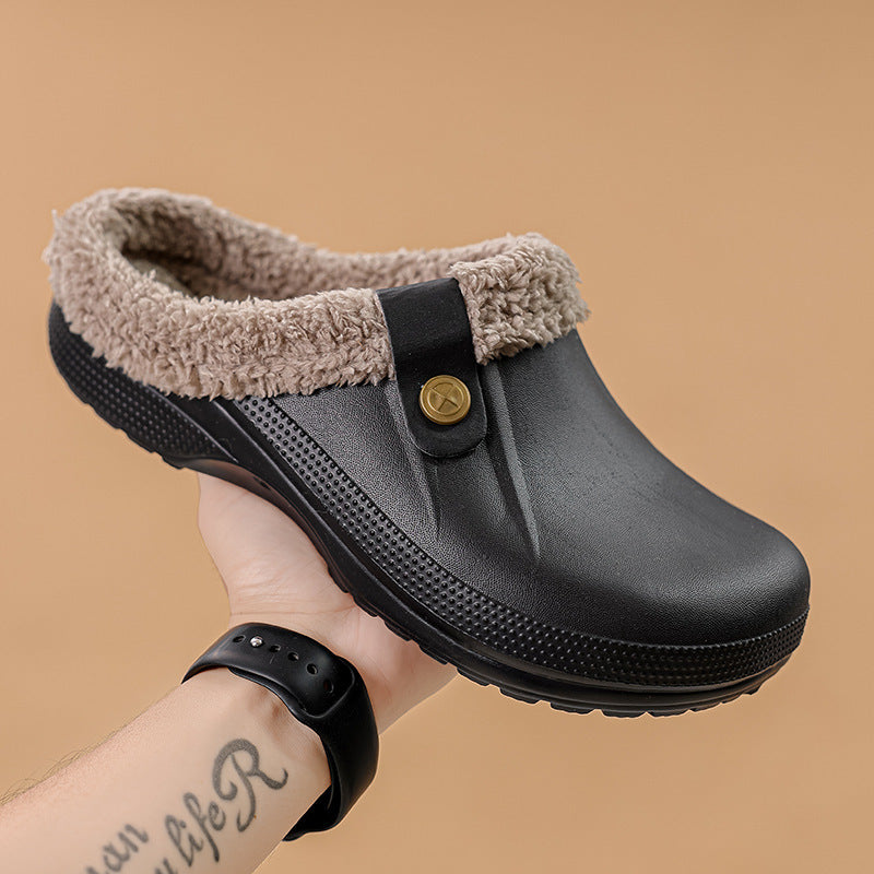 Schwarzer Clog mit beigem Fellkragen, von einer Hand vor beigem Hintergrund hochgehalten, Seitenansicht mit Riemen und Zierknopf. 2
