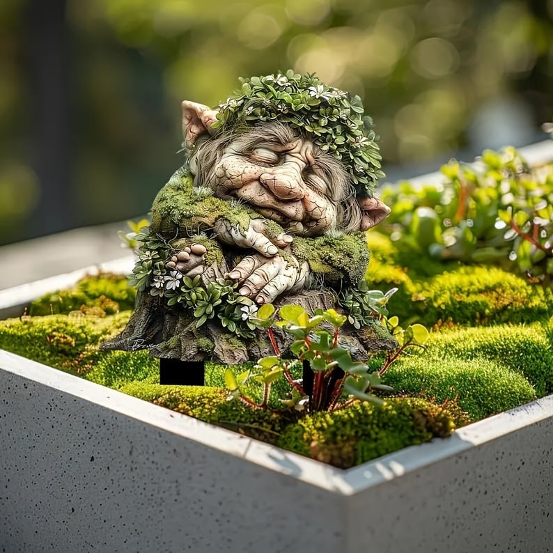 Schlafender Troll mit Blätterkranz und gefalteten Händen auf einem Baumstumpf, in einem Pflanzkübel mit Moos und Sukkulenten. 4