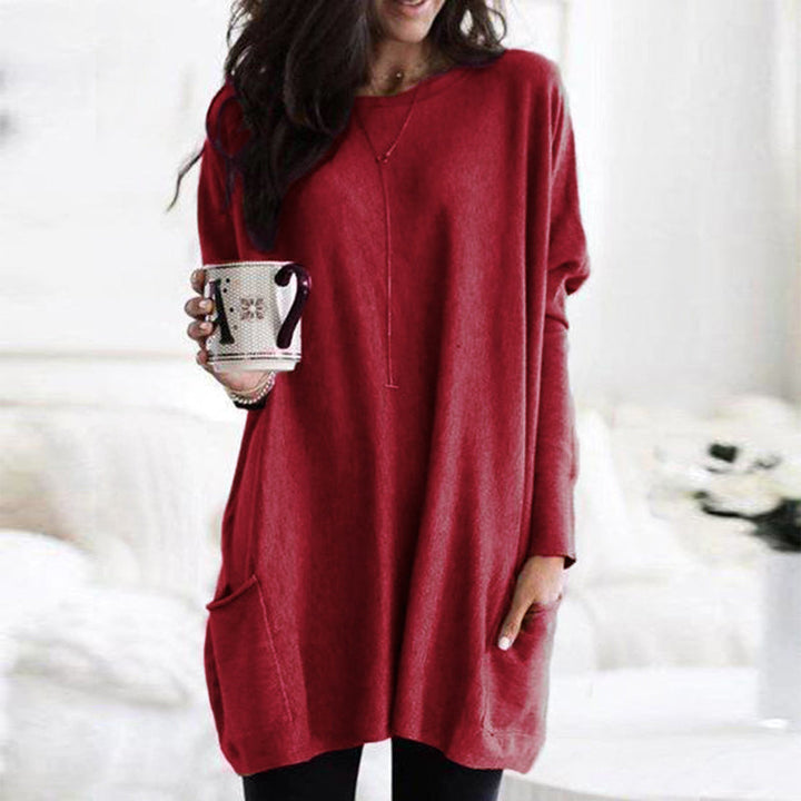 Frau in rotem Oversize-Pullover hält Tasse, gemütliche Wintermode, Wohnzimmer-Hintergrund.