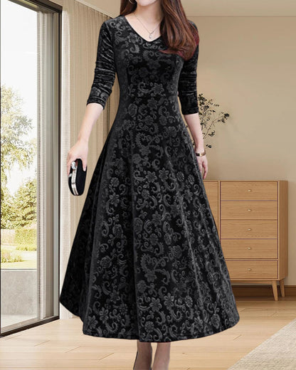 Frau in elegantem schwarzem Samtkleid mit Muster, V-Ausschnitt, 3/4-Ärmeln, in modernem Wohnzimmer.