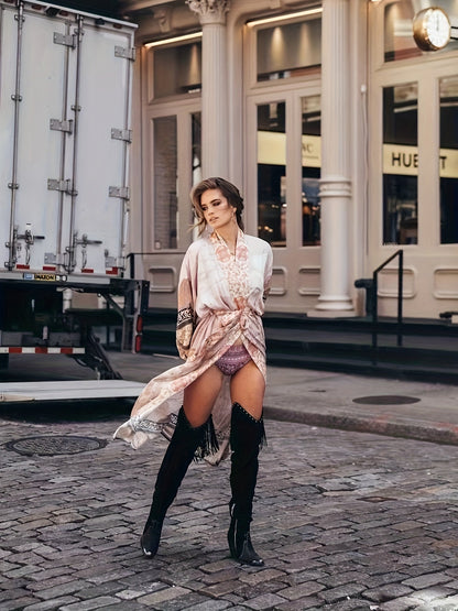 Frau in eleganter Seidenrobe und Stiefeln auf Kopfsteinpflasterstraße vor historischer Fassade.