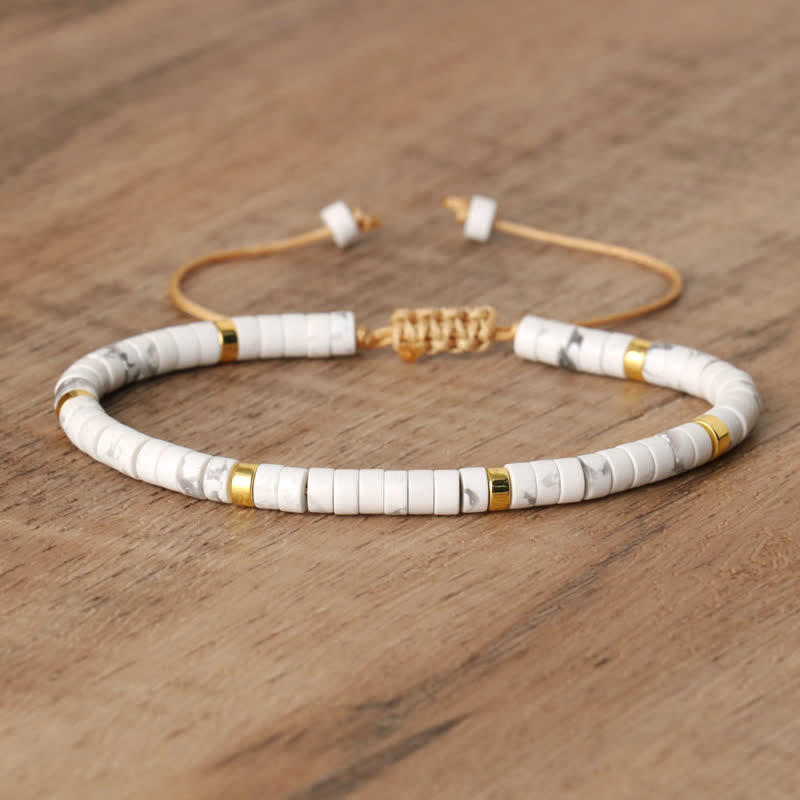 Armband aus weißen und goldenen Perlen, verstellbar, auf Holzoberfläche.
