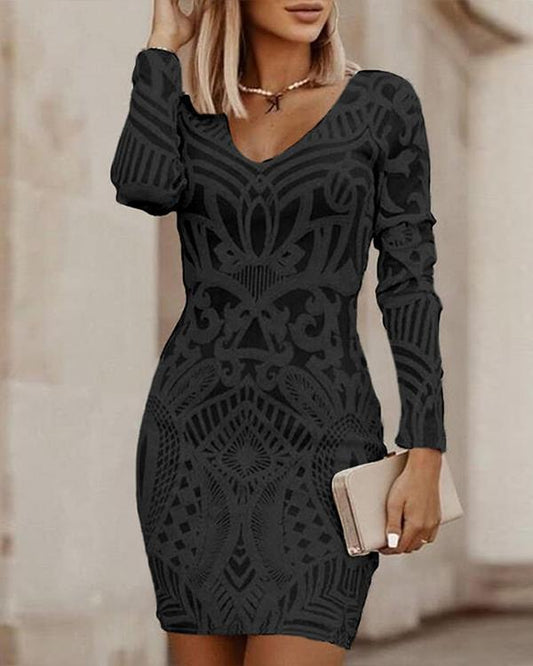Frau in schwarzem, gemustertem Kleid mit langen Ärmeln, hält eine goldene Clutch.