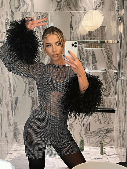 Frau im schwarzen Netzkleid mit Federärmeln, Selfie im Marmor-Badezimmer.