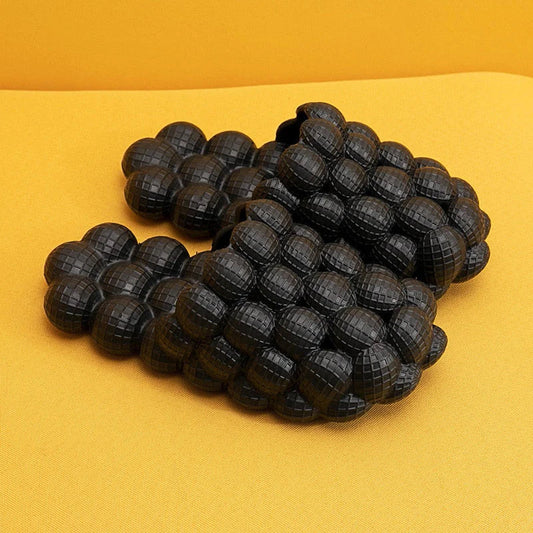 Schwarze, gepolsterte Massagesandalen auf gelbem Hintergrund, rutschfest, ergonomisch.