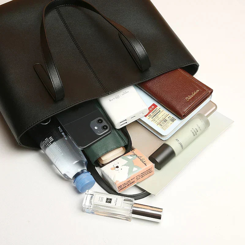 Schwarze Tote-Tasche liegend, aus der Handy, Geldbeutel, Powerbank, Flasche, Notizbuch und Kosmetik herausragen 6
