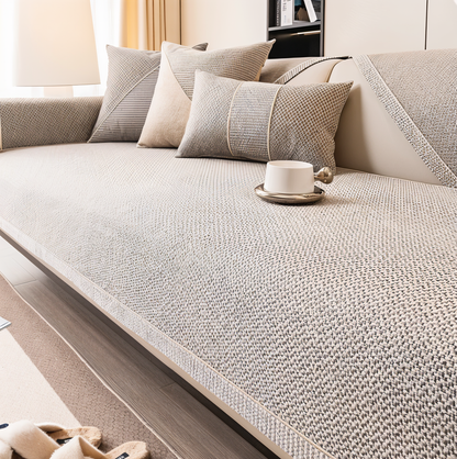 Beige-grauer Sofaschoner mit Webstruktur auf einem Sofa, dazu passende Kissen und eine weiße Tasse auf dem Sitz. 1