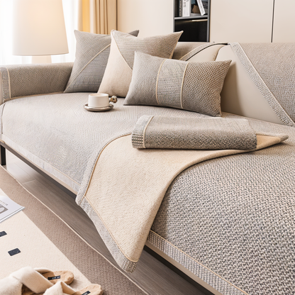Beige-grauer Sofaschoner mit zurückgeschlagenem Rand und einer gefalteten Stoffbahn, die die helle, flauschige Rückseite zeigt. 3