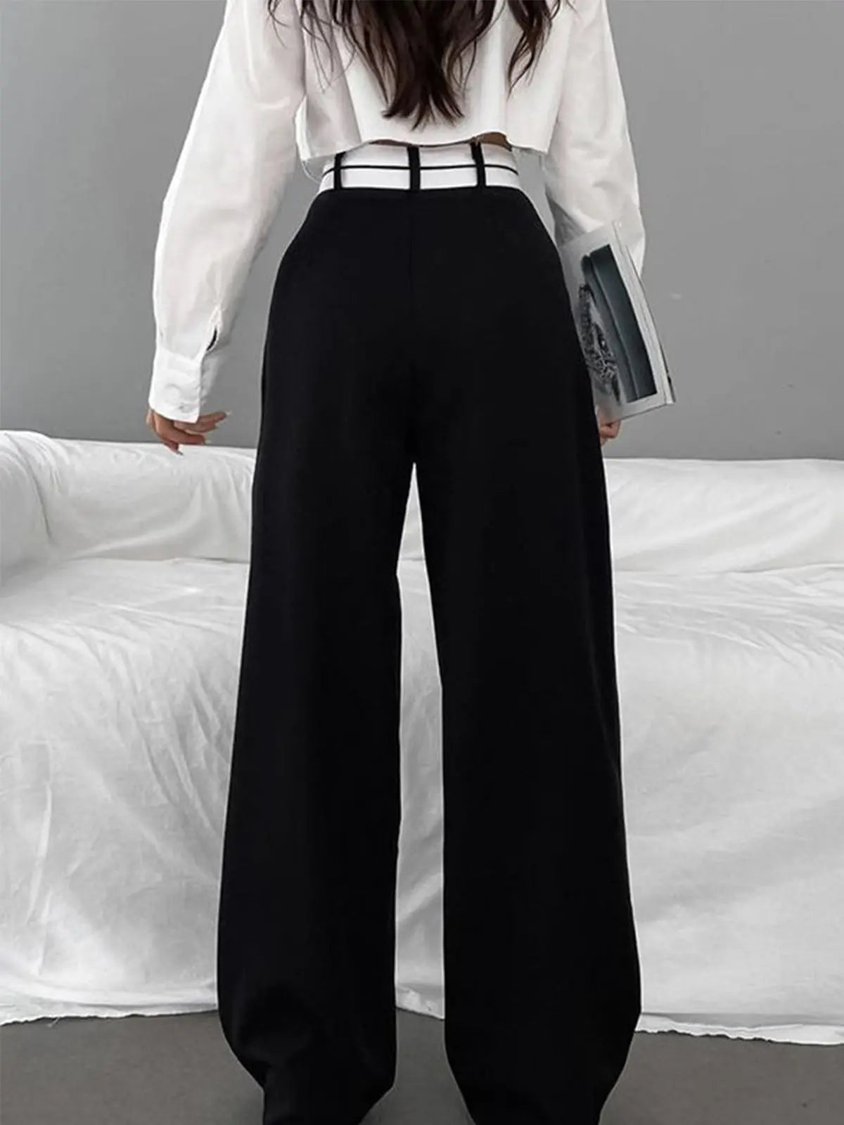 Frau in schwarzer Hose und weißer Bluse, hält Buch, moderne Mode, eleganter Look.