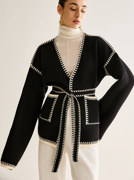 Frau trägt schwarzen Cardigan mit Gürtel, weißem Rollkragenpullover, goldenen Ohrringen.