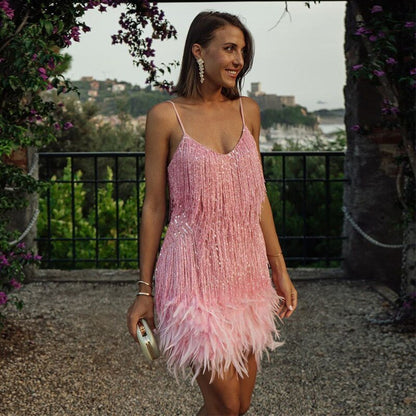 Lächelnde Frau trägt das rosa Fransenkleid mit Federsaum auf einem Kiesweg vor Blumenranken und Meerblick 1