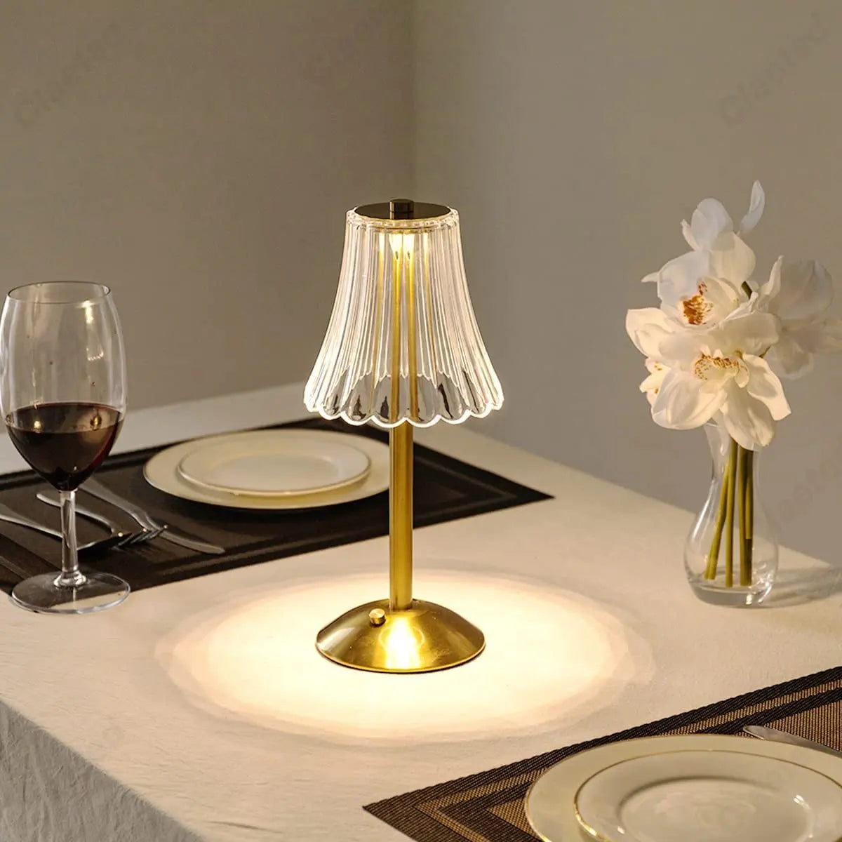 Goldene LED-Tischlampe, kabellos, wiederaufladbar, auf Esstisch mit Weinglas und Blumen.