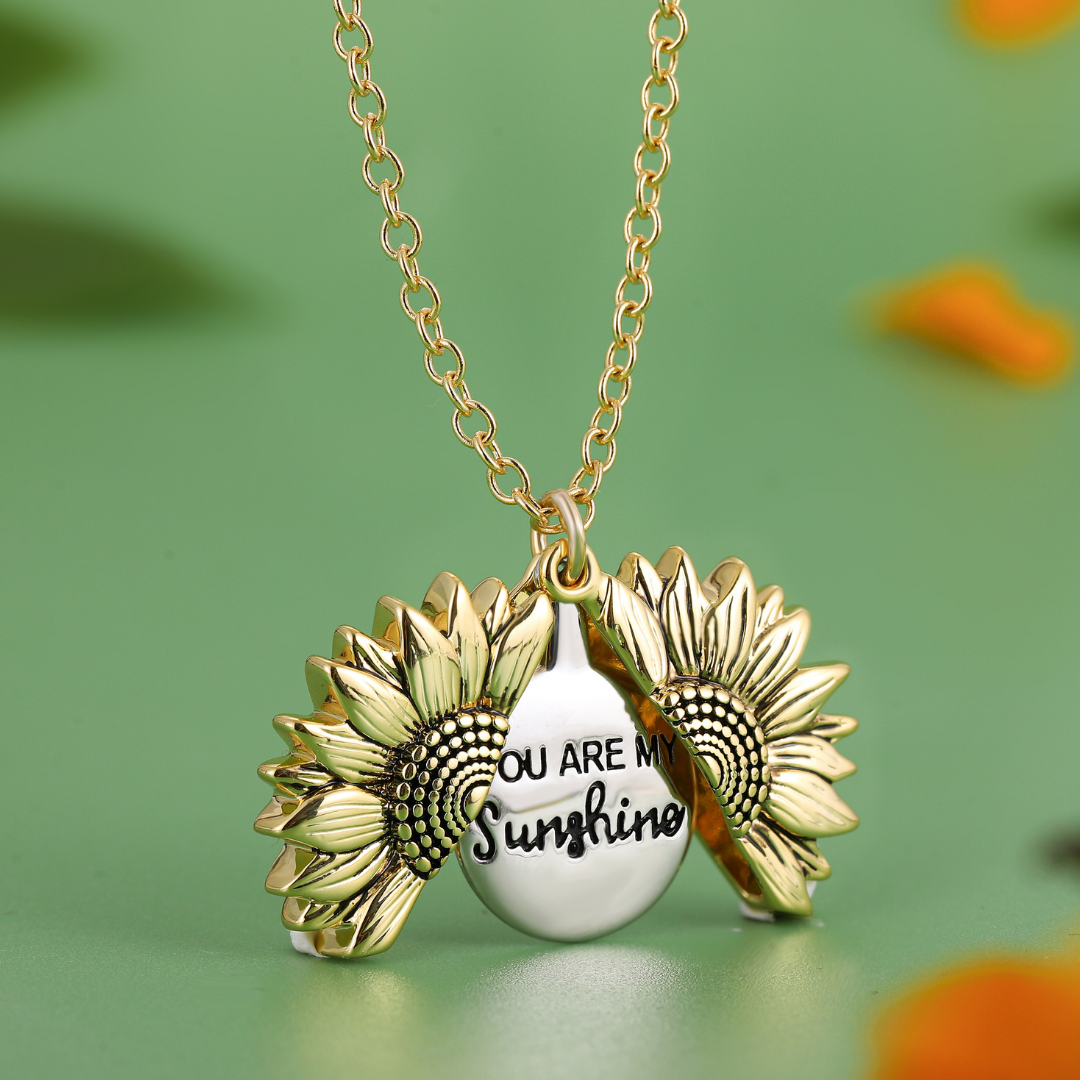 Goldene Sonnenblumen-Halskette mit "You Are My Sunshine"-Gravur auf grünem Hintergrund.