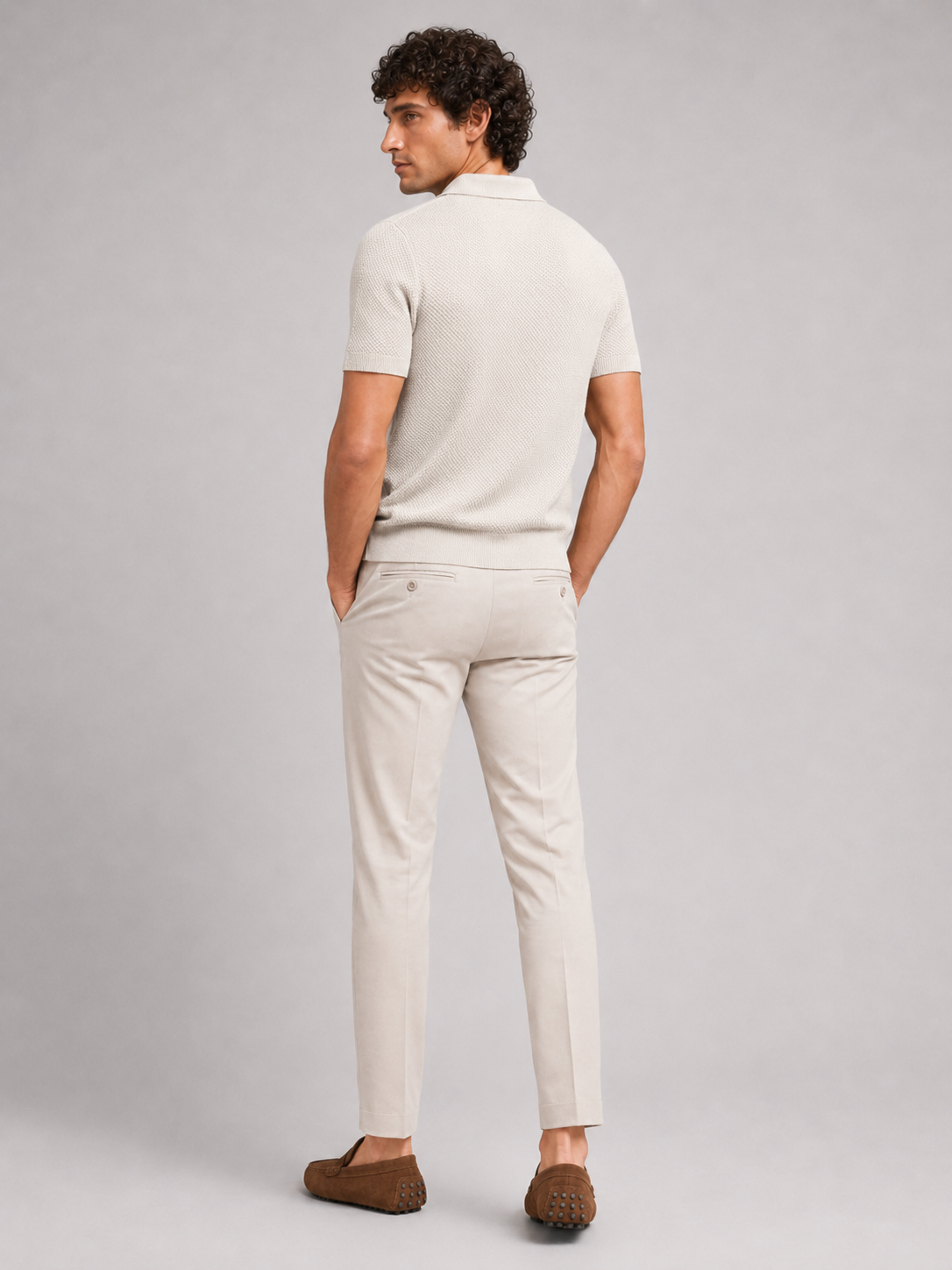 Rückansicht des cremefarbenen Poloshirts am Model, helle Hose mit Gesäßtaschen und braune Mokassins, Kopf zur Seite gedreht 19