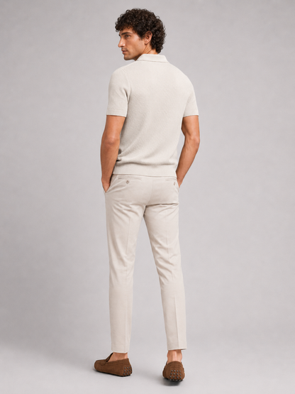 Rückansicht des cremefarbenen Poloshirts am Model, helle Hose mit Gesäßtaschen und braune Mokassins, Kopf zur Seite gedreht 19
