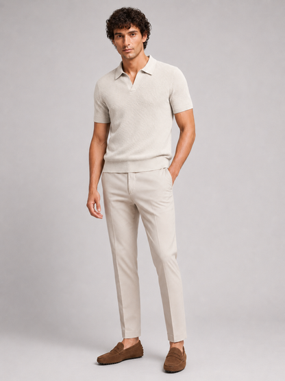 Ganzkörperfoto von vorne: cremefarbenes Strick-Poloshirt, helle Hose und braune Wildleder-Loafer vor grauem 18