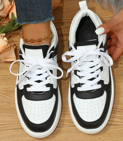 Schwarz-weiße Sneaker aus Leder auf Holzfußboden, Damenmode, Freizeitschuhe.