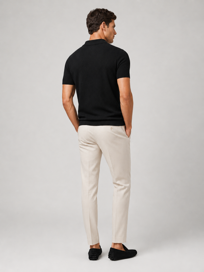 Rückansicht des schwarzen Poloshirts am Model, mit heller Hose und schwarzen Mokassins, Kopf leicht zur Seite gedreht 9