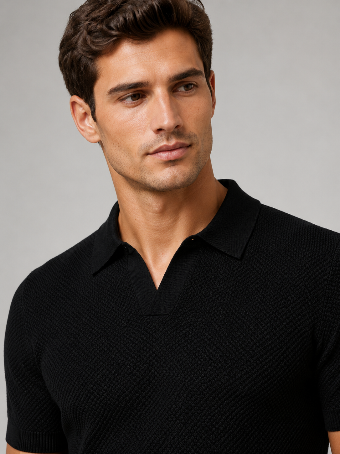 Nahaufnahme des schwarzen Poloshirts mit Kragen, V-Ausschnitt und gleichmäßiger Waffelstruktur, Model blickt zur Seite 7