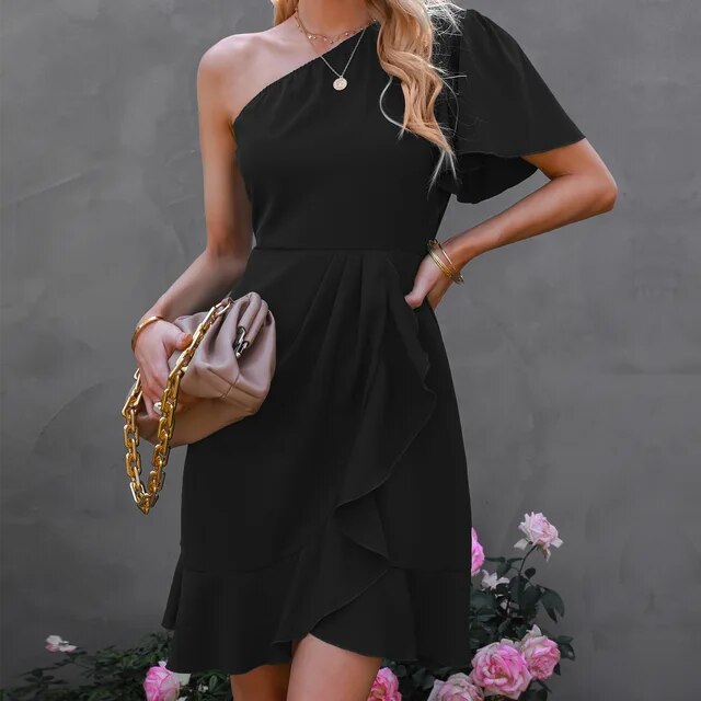 Frau in schwarzem One-Shoulder-Kleid mit Tasche, elegante Mode, vor grauem Hintergrund.
