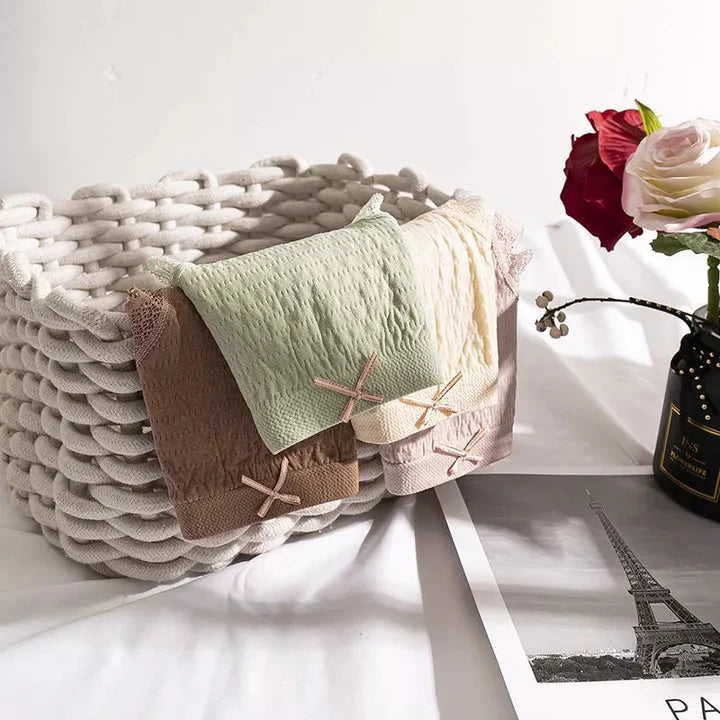 Weiße Strickkorb mit bunten Damenunterwäsche, Rosen in Vase, Eiffelturm-Foto auf Tisch.