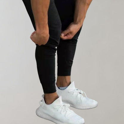 Mann in schwarzen Jogginghosen und weißen Sneakers, Sportbekleidung, Fitnessmode.