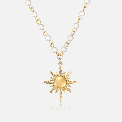 Frontansicht der Halskette: goldener Sonnenanhänger mit geschwungenen Strahlen an einer Kette aus weißen Perlen und goldenen Gliedern vor hellem Hintergrund. 1