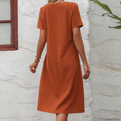 Frau in orangefarbenem Leinenkleid, knielang, vor weißer Wand, Sommermode.