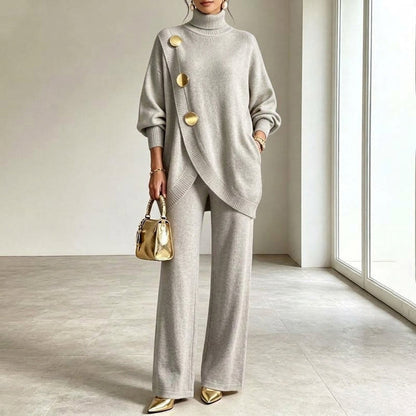 Das Strickset in hellem Grau am Model, asymmetrisch überlappendes Oberteil mit drei goldenen Knöpfen und weit fallende Hose. 3