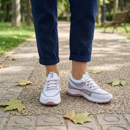 Weiße Mesh-Sneaker mit rosa Sohle an den Füßen einer Frau in dunkelblauer Hose auf gepflastertem Parkweg 20