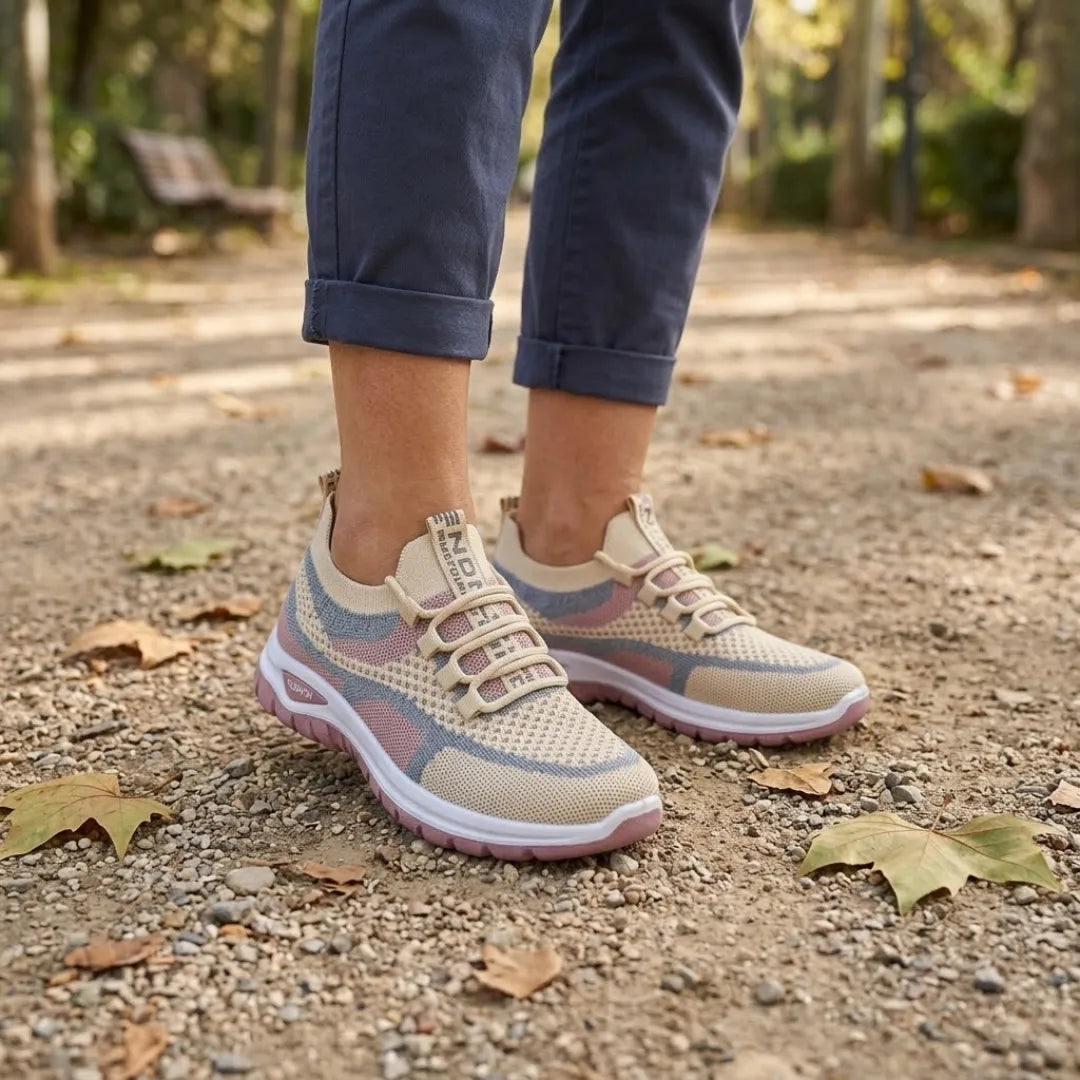 Beige Mesh-Sneaker mit rosa Akzenten, getragen von einer Person in gerollter dunkelblauer Hose auf einem Parkweg mit Herbstlaub. 29