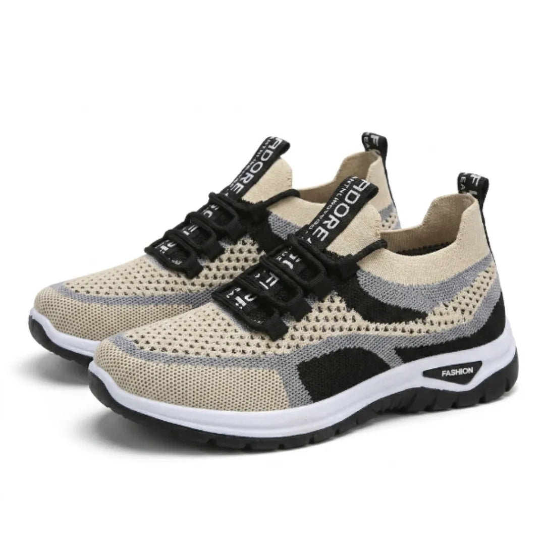 Paar beige Mesh-Sneaker mit grauen und schwarzen Akzenten, schwarzen Schnürsenkeln und weißer Sohle, schräg von vorn auf weißem Hintergrund. 43