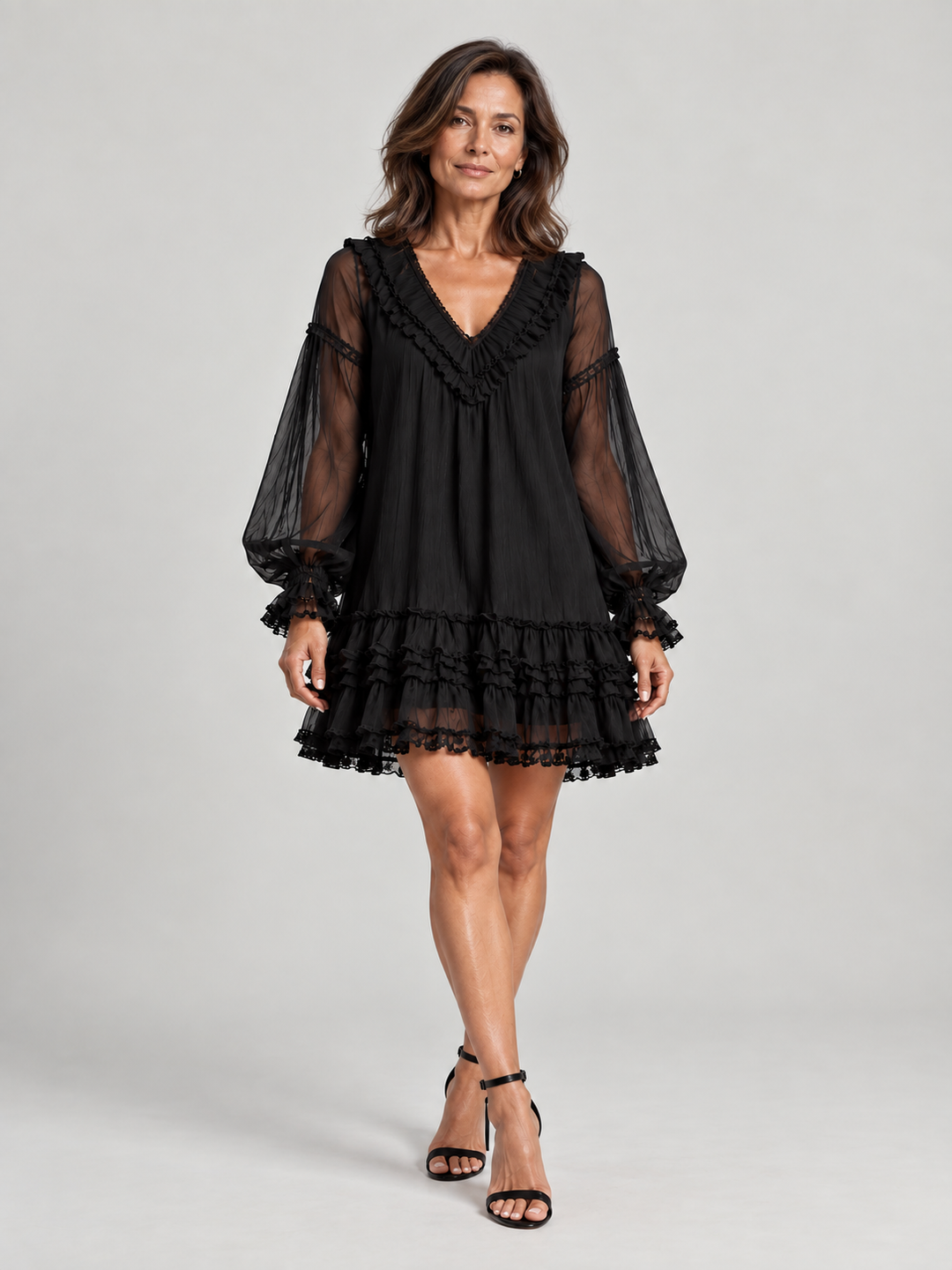 Ganzkörperansicht von vorn: Das schwarze Rüschenkleid mit transparenten Ärmeln wird mit schwarzen Sandaletten mit Absatz getragen. 2