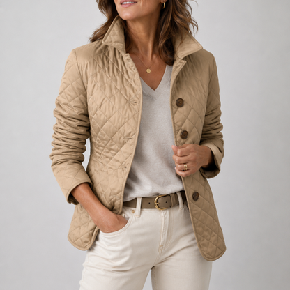 Beige Steppjacke mit Rautenmuster, getragen über hellem V-Ausschnitt-Pullover, Gürtel und heller Hose vor grauem Hintergrund 1
