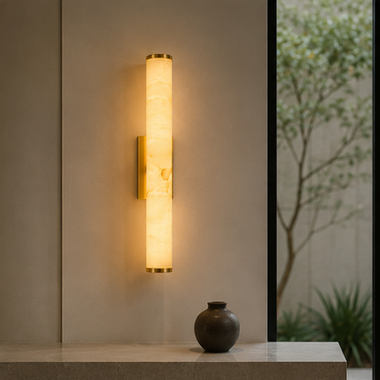 Wandlampe mit goldfarbenen Kappen und Halterung über einer Steinablage mit dunkler Vase, neben einem Fenster mit Blick auf Bäume. 10