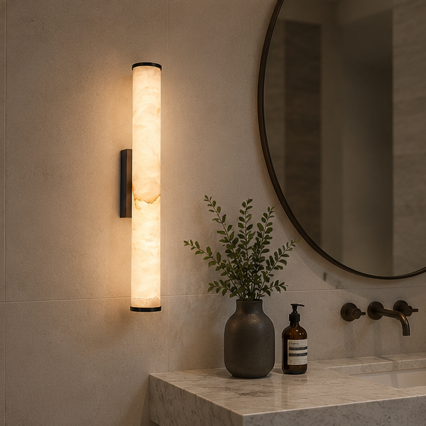 Wandlampe mit schwarzen Endkappen und marmoriertem Leuchtzylinder im Badezimmer neben rundem Spiegel, Marmorwaschtisch, Vase und Seifenspender. 4