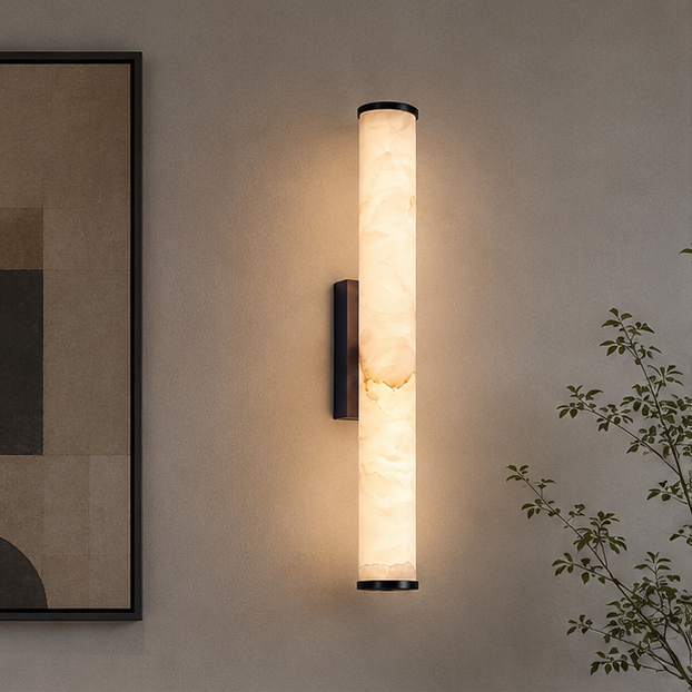Wandlampe mit marmoriertem Zylinder und schwarzen Kappen leuchtet warm an einer beigen Wand neben einem Bild und einem Zweig. 3