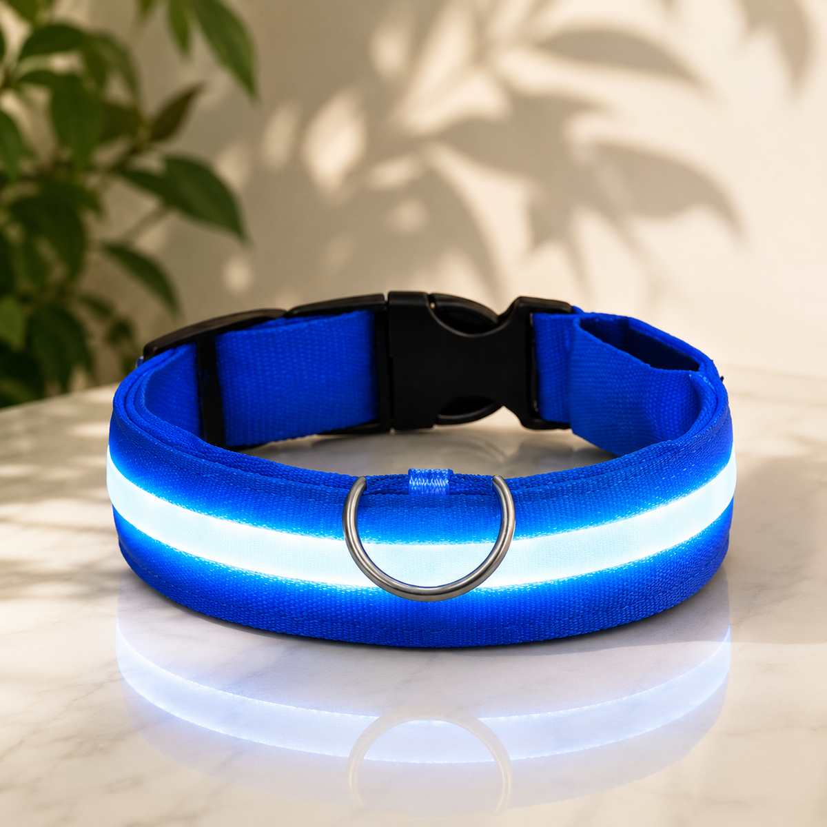 Blaues Nylon-Halsband mit leuchtendem Streifen, Steckschnalle und D-Ring auf heller Marmorfläche vor Pflanzenschatten. 1
