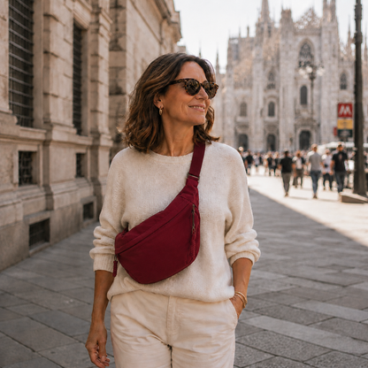 Lächelnde Frau mit Sonnenbrille trägt die bordeauxfarbene Tasche diagonal vor dem Körper, im Hintergrund eine belebte Altstadt mit gotischer Kathedrale. 4