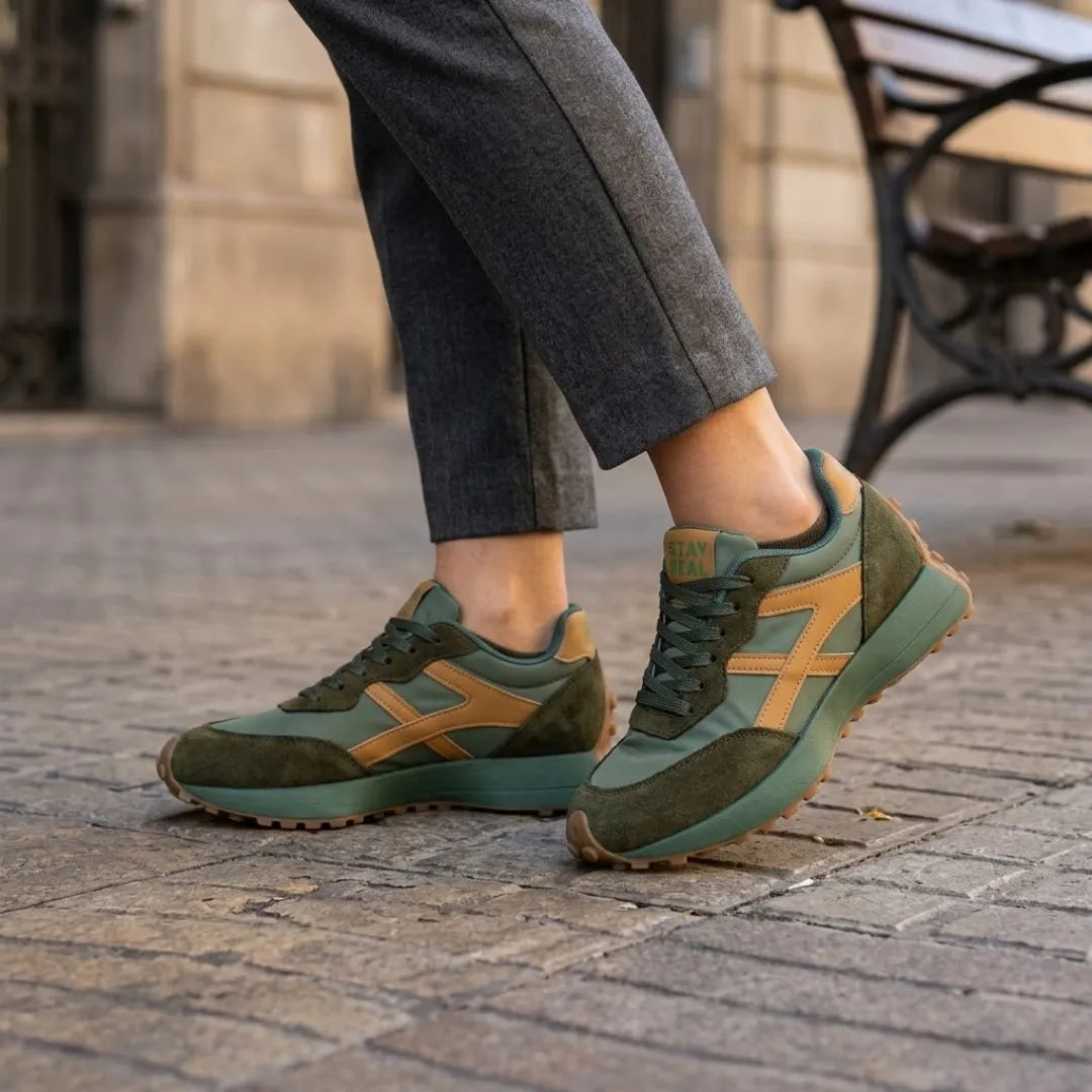 Grüne Sneaker mit ockerfarbenen Streifen, getragen zu grauer Hose auf Kopfsteinpflaster 12