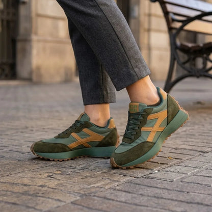 Grüne Sneaker mit ockerfarbenen Streifen, getragen zu grauer Hose auf Kopfsteinpflaster 12