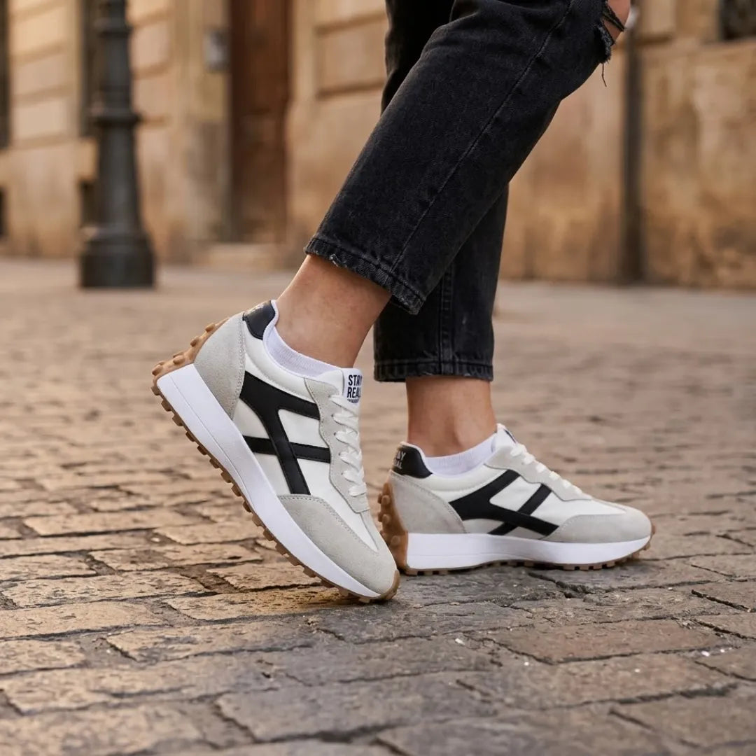 Sneaker getragen von einer Frau mit schwarzer Jeans und weißen Socken auf Kopfsteinpflaster 22