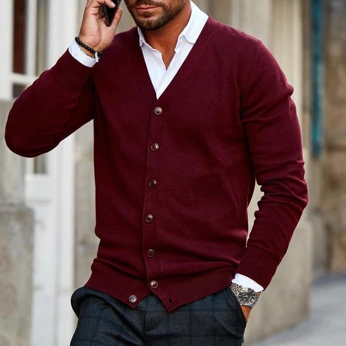 Mann in bordeauxroter Strickjacke über weißem Hemd telefoniert, eine Hand in der karierten Hose, Knopfleiste und gerippter Saum sichtbar. 1