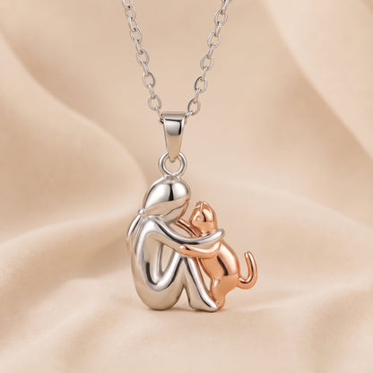 Silberfarbene Figur mit roségoldfarbener Katze, die die Pfoten an sie legt, Anhänger an Kette auf Stoff. 4