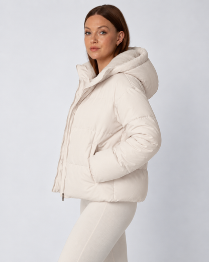 Seitenansicht der cremefarbenen Jacke mit aufgesetzter Kapuze, Hände in den seitlichen Taschen 3