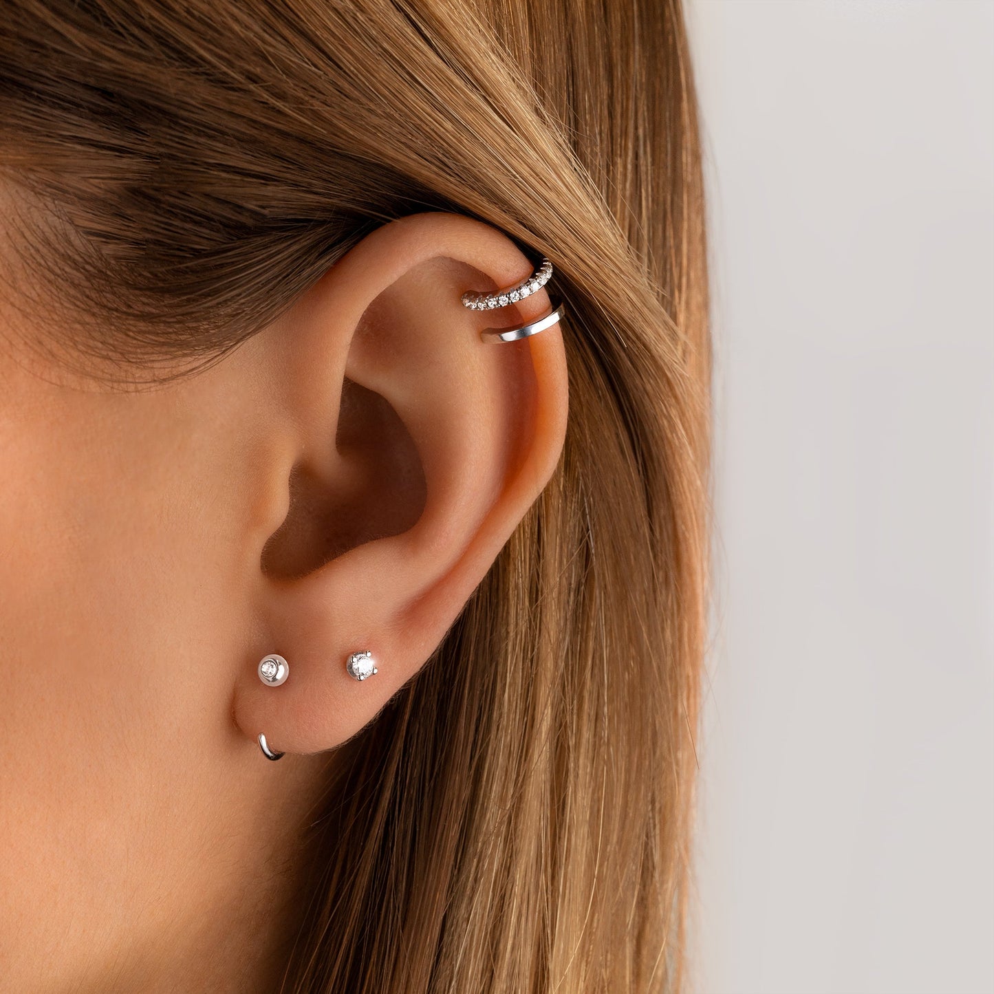 Frauenohr mit mehreren silbernen Ohrringen und Ohrklemmen, minimalistisch, Schmucktrends.
